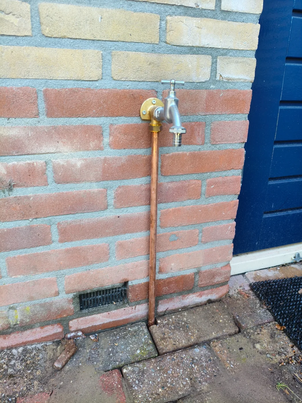 Buitenkraan met koperen leidingwerk op een buitengevel